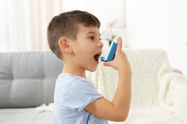 Criança utilizando inalador para tratar asma, ilustrando o controle dos sintomas respiratórios comuns da asma infantil.