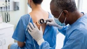 Médico realizando exame dermatológico em pinta nas costas de paciente, ilustrando a avaliação e prevenção do câncer de pele por meio do diagnóstico precoce.