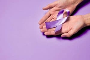 Mãos segurando laço roxo de conscientização sobre Hanseníase, representando a importância da prevenção, diagnóstico precoce e tratamento da doença.