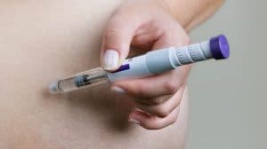 Pessoa aplicando caneta injetável na região abdominal, representando o uso de Mounjaro e os possíveis riscos associados ao medicamento.
