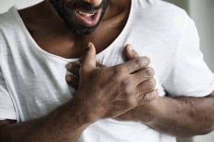 Homem segurando o peito com expressão de dor e desconforto, ilustrando sintomas associados à Síndrome de Takotsubo, também conhecida como síndrome do coração partido.