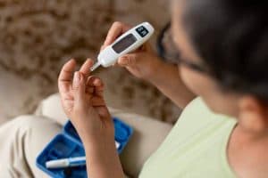 Pessoa realizando teste de glicemia com medidor digital e coleta de sangue na ponta do dedo, ilustrando os cuidados e o acompanhamento do diabetes tipo 5.