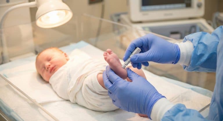 Profissional de saúde realizando o teste do pezinho em recém-nascido, exame essencial para identificar precocemente doenças congênitas e proteger a saúde do bebê.