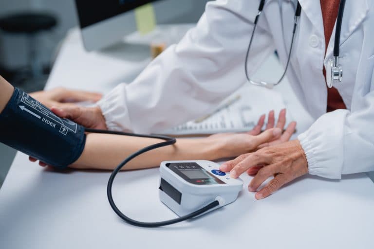 Profissional de saúde aferindo a pressão arterial de um paciente durante consulta, etapa importante antes de iniciar exercícios físicos para quem tem pressão alta e diabetes.