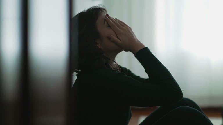 Mulher sentada com as mãos sobre o rosto, demonstrando sofrimento emocional, representando a depressão e a importância de oferecer apoio a quem enfrenta a condição.