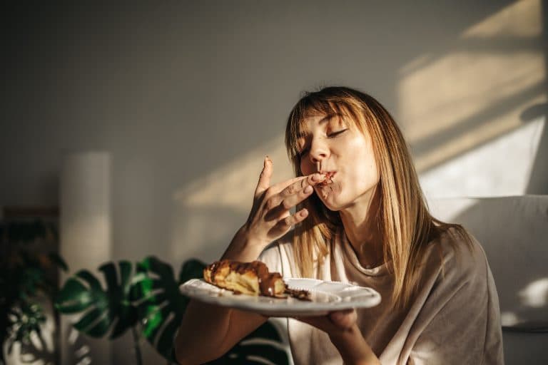 Mulher comendo um pedaço de bolo, representando a sensação de fome frequente e a vontade de comer ao longo do dia.