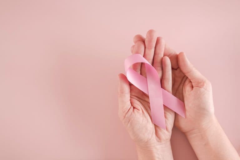 Mãos segurando um laço rosa, símbolo da conscientização sobre o câncer de mama, destacando a importância do cuidado contínuo com a saúde das mamas e da prevenção ao longo do ano.