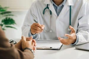 Médico em consulta conversando com paciente e apontando informações em um prontuário, representando o diagnóstico, orientação e tratamento do Linfoma de Hodgkin.