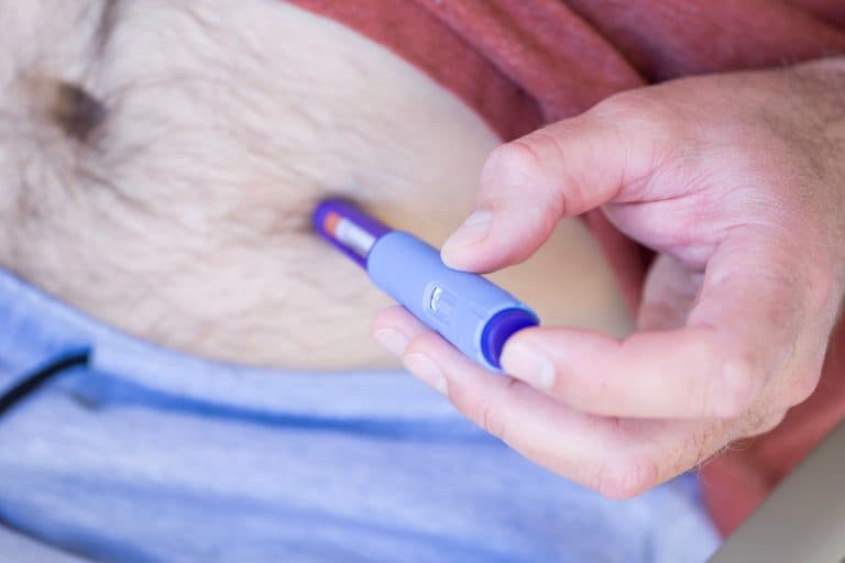 Pessoa aplicando uma caneta emagrecedora na região abdominal, ilustrando o uso de medicamentos injetáveis para controle do peso que exigem acompanhamento médico e avaliação de um endocrinologista.