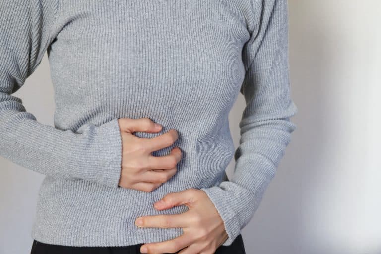 Pessoa segurando a região abdominal com expressão corporal de desconforto, ilustrando sintomas associados às doenças inflamatórias intestinais, como dor abdominal, cólicas e alterações digestivas.