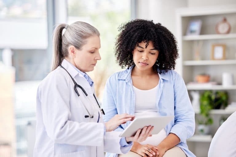 Médica apresenta informações em um tablet durante consulta com paciente, ilustrando a investigação diagnóstica e o acompanhamento dos sintomas relacionados à SOMP (Síndrome Ovariana Metabólica Poliendócrina).