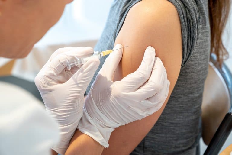 Profissional de saúde aplicando a vacina da gripe no braço de uma paciente, destacando a importância da imunização para prevenir complicações da influenza.