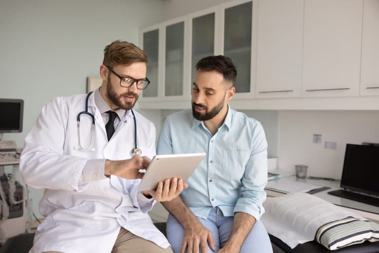 Médico orienta um paciente durante consulta, utilizando um tablet para explicar informações sobre prevenção, diagnóstico e tratamento da leishmaniose.