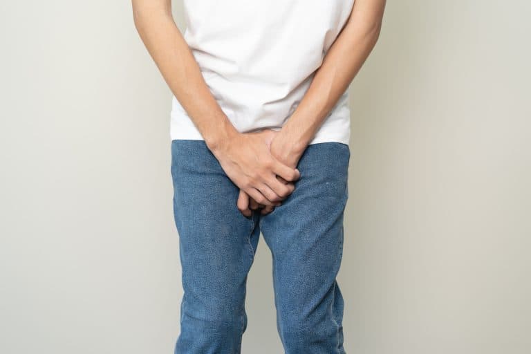 Pessoa segura a região pélvica com as mãos, ilustrando desconforto e dificuldade para urinar, um sintoma que pode indicar alterações no trato urinário e merece investigação médica.