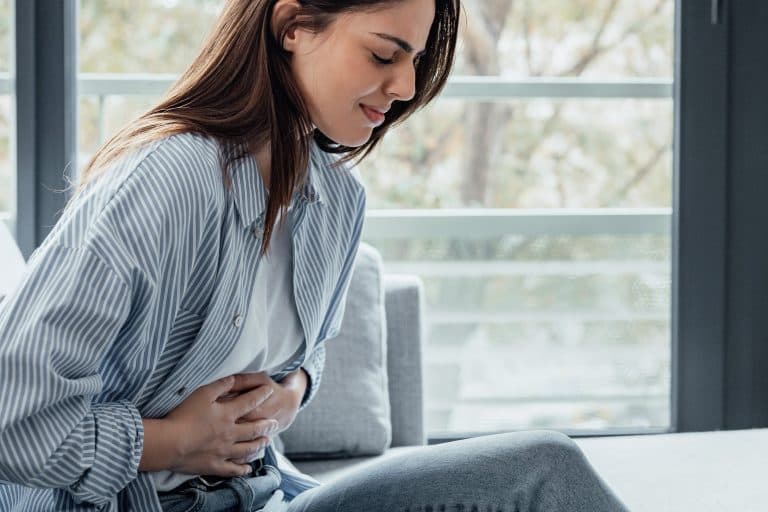 Pessoa sentada segura a região superior do abdômen com expressão de dor, ilustrando um dos principais sintomas da pancreatite, condição que exige avaliação médica e tratamento adequado.
